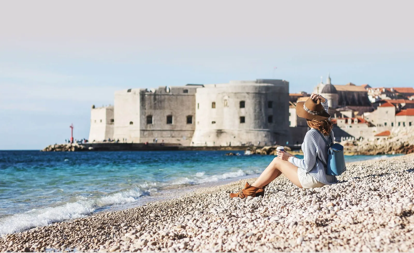 A traveler relaxing on a pebble beach below Dubrovnik's old town walls